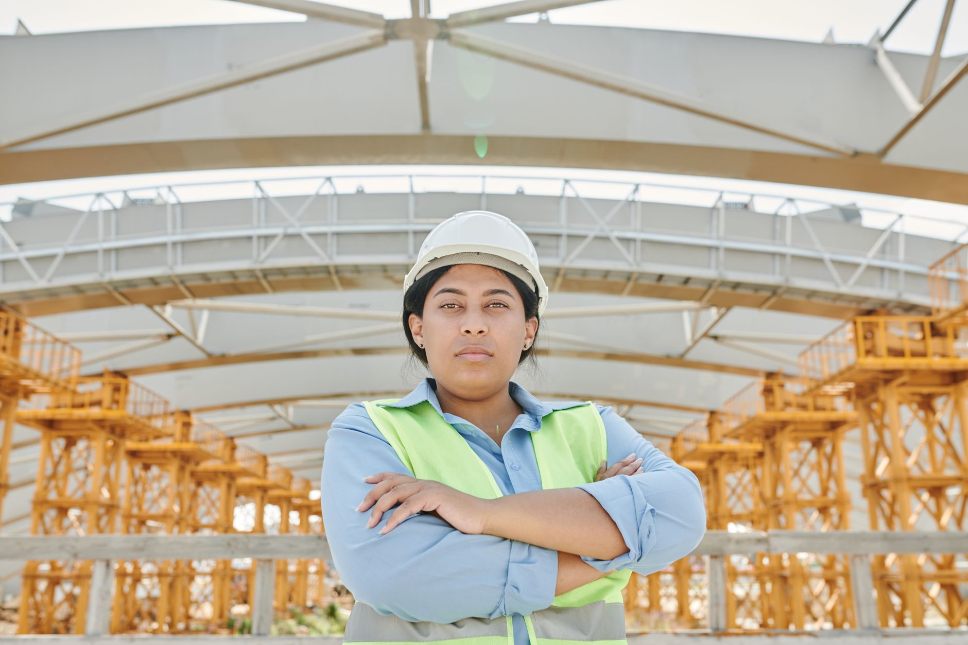 Female engineer in safety gear at a construction site with steel structure background.